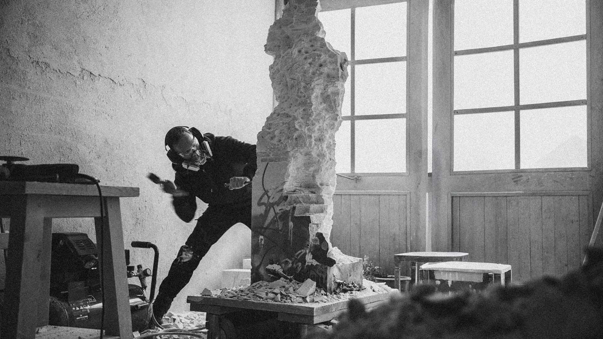 Schwarzweiße Aufnahme von Jonas Eideloth bei der Arbeit an einer hohen Skulptur