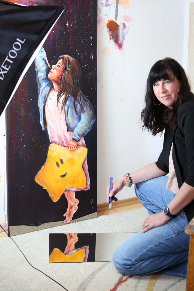 Sigrid Platzer kniet im Atelier neben Lucy; vor ihr liegt ein Spiegel, in dem sich das Gemälde spiegelt